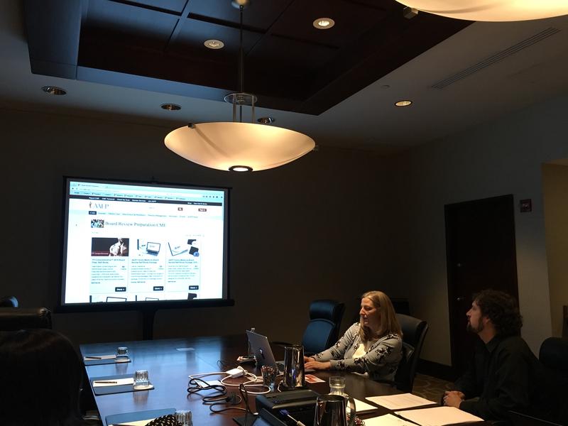 Picture of a usability test where the participant sits beside the faciliator while their screen is being projected on a screen for observers to watch.